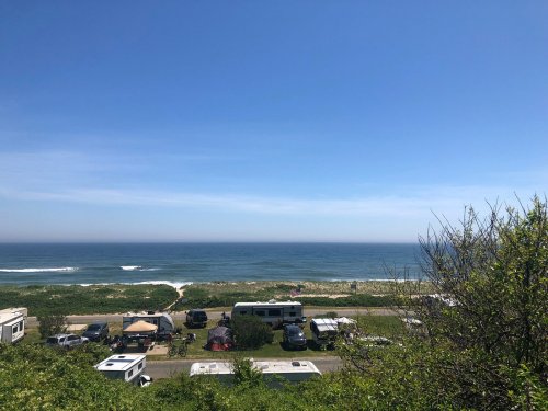 A scenic view of the ocean with RVs parked along the shore under a clear blue sky.
