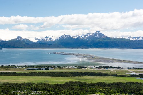 A scenic view of mountains, a calm bay, and a small coastal town under a clear blue sky.