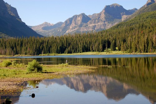 A serene lake surrounded by mountains and dense forests, reflecting the landscape in calm waters.