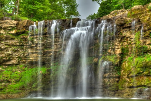 A serene waterfall cascading over rocky cliffs, surrounded by lush green trees and a calm pool below.