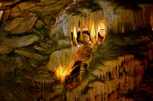 Stalactites and stalagmites illuminated in a cave, showcasing intricate rock formations and warm lighting.