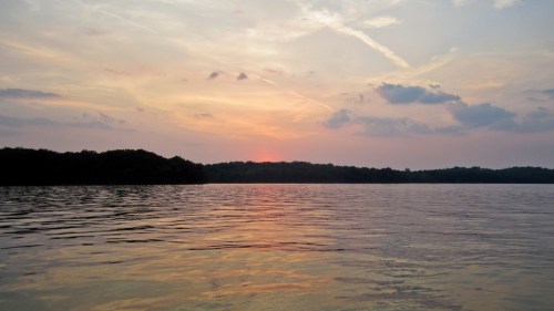 A serene sunset over a calm lake, with soft clouds and reflections on the water's surface.