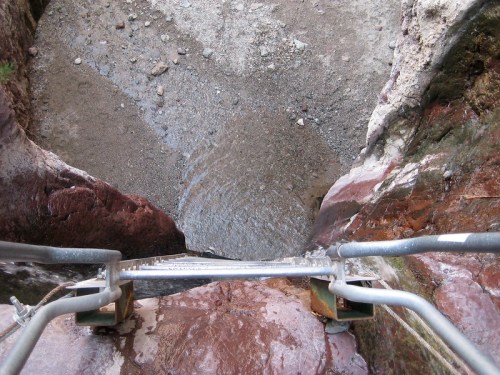 View from a metal ladder looking down into a rocky crevice with water at the bottom.