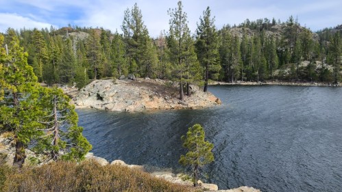 A serene lake surrounded by rocky shores and tall pine trees under a clear blue sky.