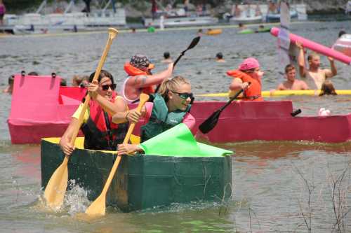 Participants paddle colorful cardboard boats in a lively water race, enjoying a sunny day on the lake.