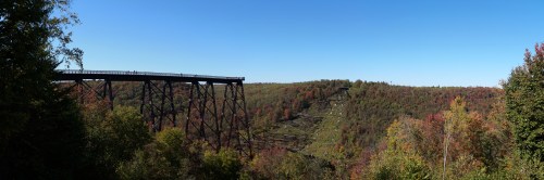 A panoramic view of a trestle bridge over a colorful autumn landscape with rolling hills and clear blue sky.