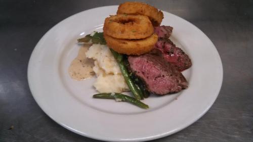 A plate of sliced beef, mashed potatoes, green beans, and onion rings, garnished with gravy.
