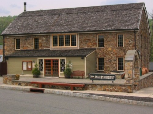 A stone and wood building with large windows, featuring a sign for "Dog Valley Pub & Brewery" in a scenic setting.