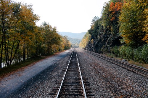 A view of two parallel railway tracks surrounded by autumn foliage and mountains in the background.