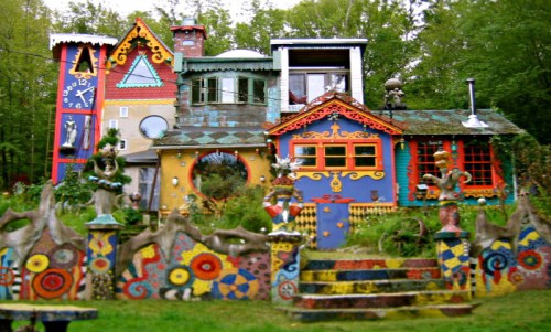 A colorful, whimsical house with unique architectural features and vibrant decorations surrounded by lush greenery.
