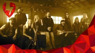 A group of musicians posing together in a rustic setting, with guitars and a vintage vibe.