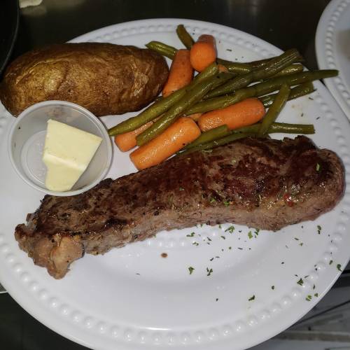A plate with a grilled steak, baked potato with butter, and a side of green beans and carrots.
