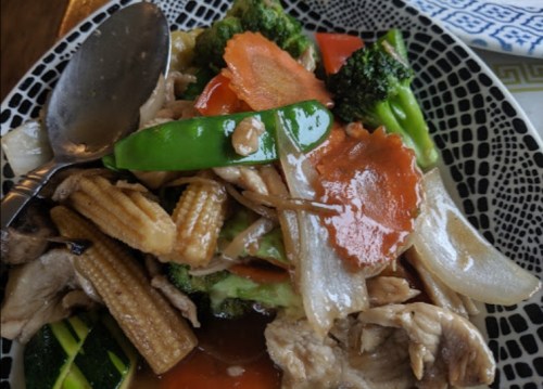 A colorful plate of stir-fried vegetables and chicken, featuring broccoli, carrots, and baby corn in a savory sauce.