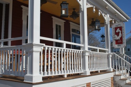 A charming porch with white railings and lanterns, featuring a sign for "Matt's Red Rooster Grill."