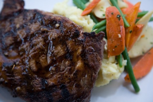 A grilled steak served with mashed potatoes and a mix of green beans, carrots, and sliced apples.