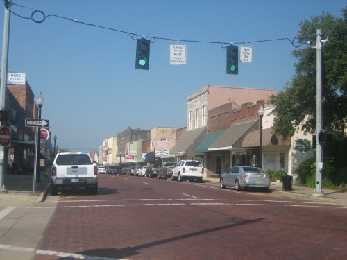 A quiet downtown street with brick pavement, shops, and traffic lights on a clear day.