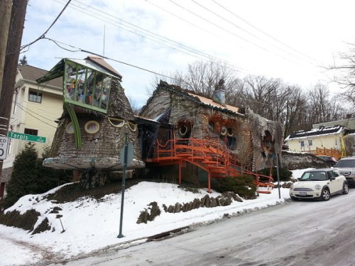 Whimsical, colorful house with unique architecture, surrounded by snow and trees, located on a quiet street.