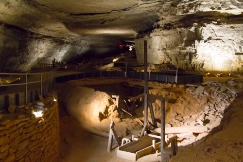 A dimly lit cave interior with rock formations, pathways, and excavation equipment scattered on the ground.