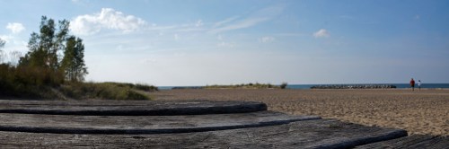 A serene beach scene with wooden steps leading to the sand, gentle waves, and two people walking in the distance.