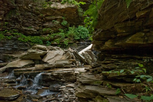 A serene rocky landscape with a small waterfall and lush greenery among layered stone formations.