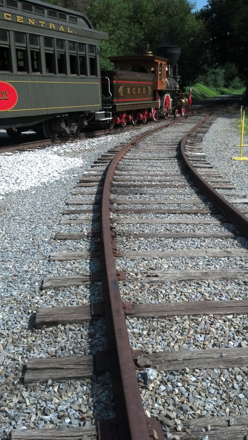 A vintage steam train on a curved track, surrounded by greenery and gravel.