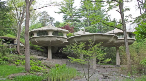 Two futuristic, saucer-shaped houses on stilts surrounded by greenery and trees.
