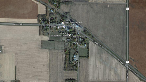 Aerial view of a rural area featuring roads, fields, and a small cluster of buildings.