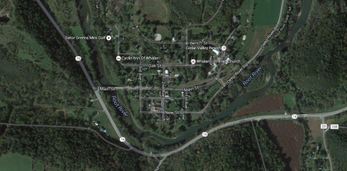 Aerial view of a small town with roads, buildings, and surrounding greenery near a river.