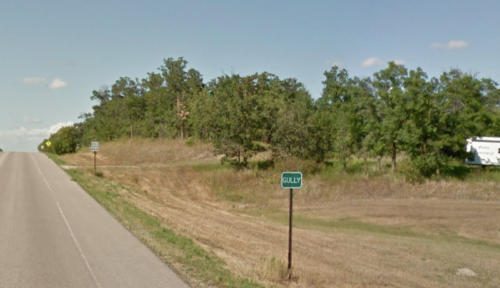A rural road with a sign for "Gully" and trees lining the roadside under a clear blue sky.