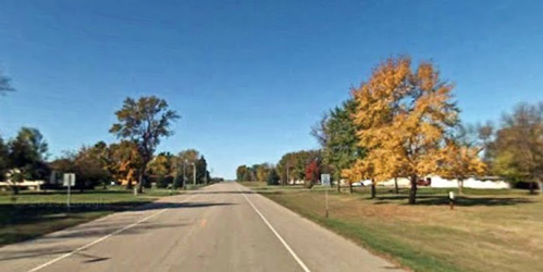 A quiet rural road lined with trees displaying autumn colors under a clear blue sky.
