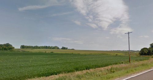 A wide view of green fields under a cloudy sky, with a telephone pole along the roadside.