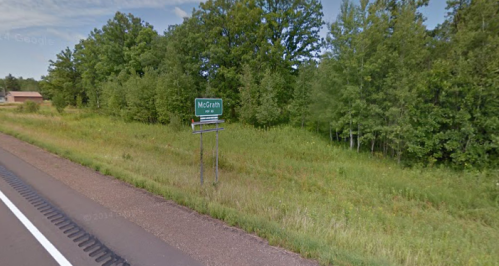 Sign for McGrath along a highway, surrounded by green trees and grass. Clear blue sky in the background.