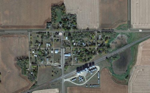 Aerial view of a small rural community with fields, roads, and a cluster of buildings.