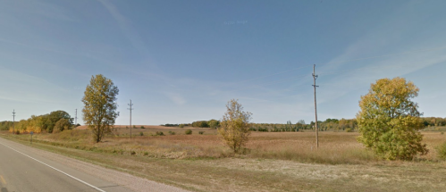 A wide view of a rural landscape with fields, trees, and power lines under a clear blue sky.