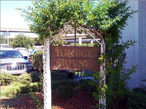A wooden sign reading "Bridge House" surrounded by greenery at an entrance.