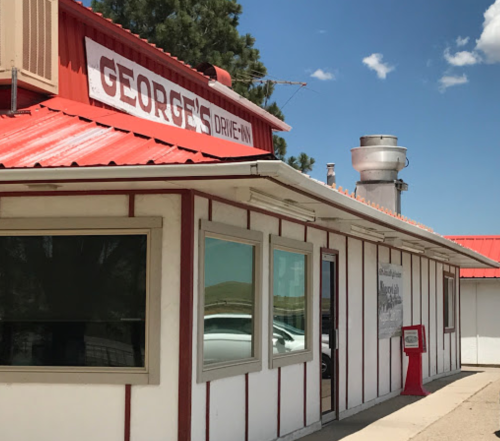 Exterior of George's Drive-In, featuring a red roof and white walls, with a vintage sign and a scenic blue sky.