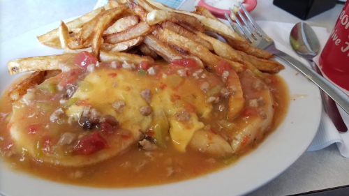 A plate of cheesy beef smothered in sauce, served with crispy French fries on the side.