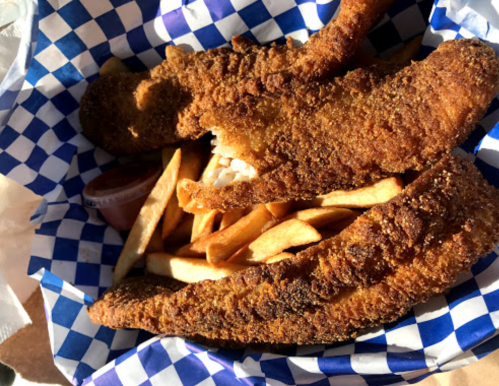 A basket of golden-brown fried fish fillets with French fries and a small container of dipping sauce.