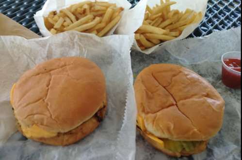 Two cheeseburgers on paper with two servings of fries and a small cup of ketchup in the background.