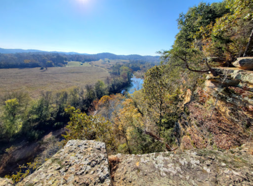 A scenic view from a rocky overlook, showcasing a river winding through lush, autumn-colored hills and valleys.