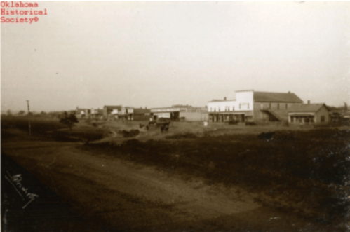 Historic black-and-white photo of a small town with buildings and dirt roads, labeled by the Oklahoma Historical Society.