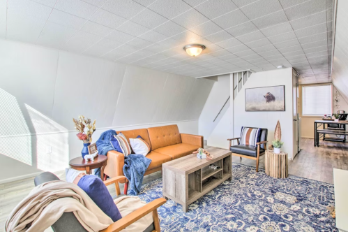 Cozy living room with an orange sofa, blue rug, wooden coffee table, and natural light from a window.