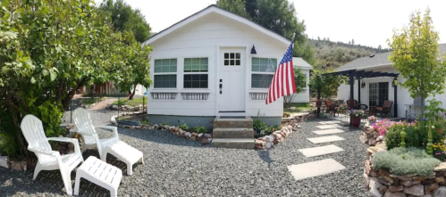 A charming white house with an American flag, surrounded by a landscaped garden and gravel pathways.