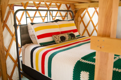 Cozy bed with colorful striped blankets inside a wooden yurt, featuring a decorative pillow.