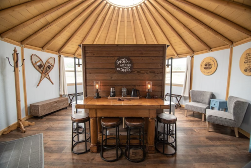 Cozy interior of a yurt featuring a wooden table, stools, and rustic decor with a circular skylight above.