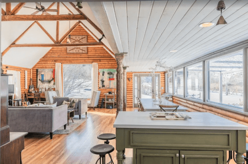 Bright, spacious interior of a rustic cabin with wooden beams, a cozy living area, and large windows.
