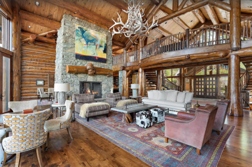 A spacious, rustic living room with wooden beams, a stone fireplace, and cozy furniture, featuring a colorful artwork.