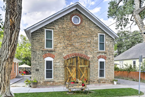 A charming stone building with wooden doors, surrounded by greenery and a gravel path.
