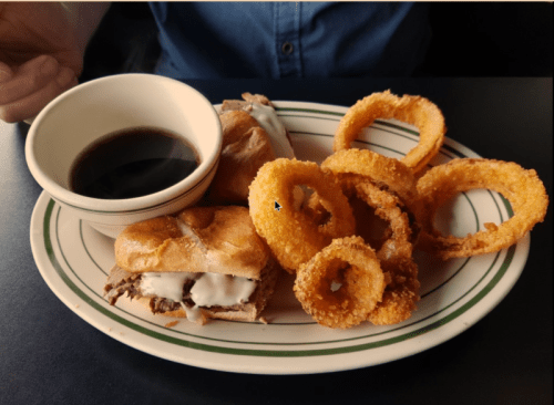 A plate with a small sandwich, dipping sauce, and crispy onion rings.