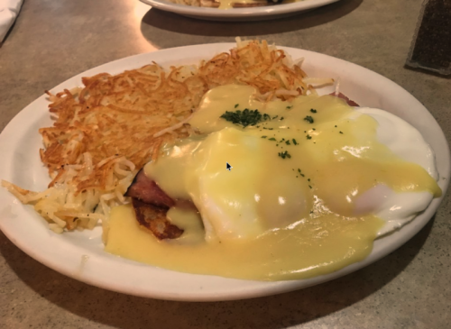A plate of eggs Benedict with poached eggs, hollandaise sauce, and crispy hash browns.